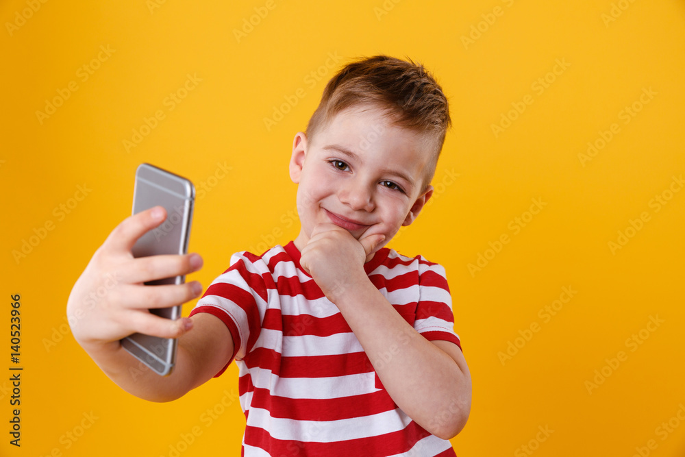 Fototapeta premium Smiling little boy making selfie and thinking about something