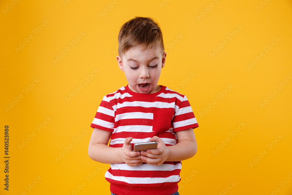 Naklejka premium Clever excited little boy reading message on mobile phone