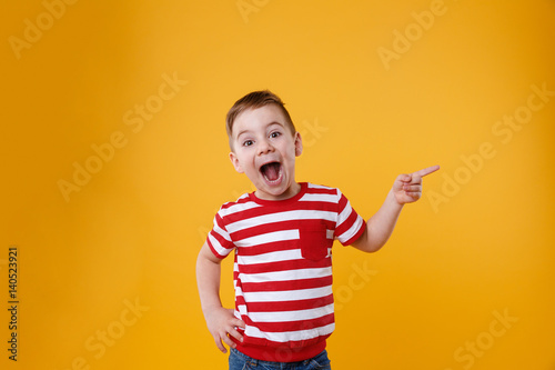 Surprised happy boy pointing fingers up at copyspace photo