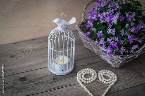 White candlestick. Wicker basket with violet flowers Campanula portenschlagiana and beautiful white pearl necklace on a wooden background. photo