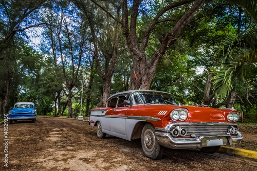 Roter Oldtimer mit blauem Oldtimer im Hintergrund in Santa Clara in Kuba - Serie Kuba Reportage