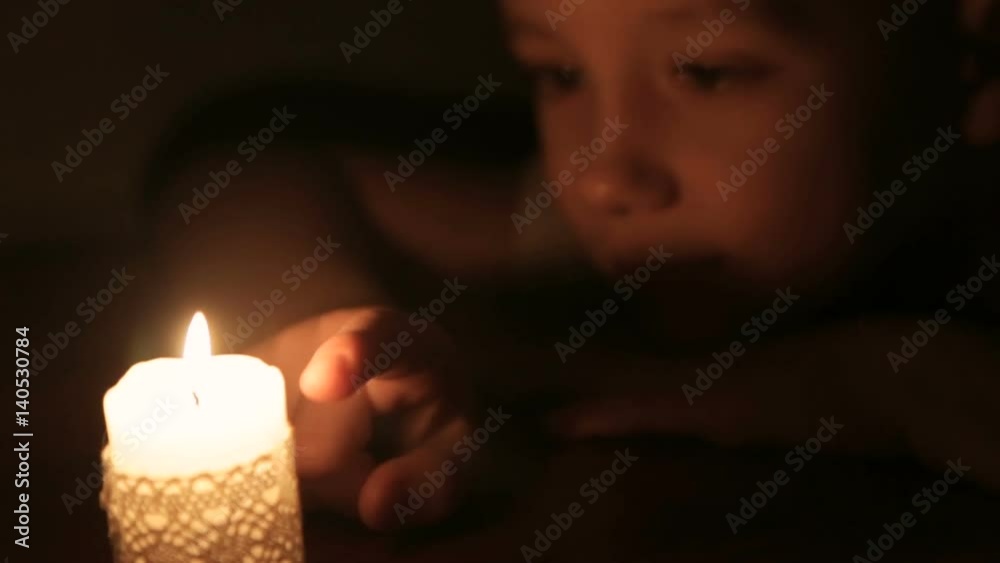 The boy touches the wax of a burning candle The boy touches the wax of a burning candle