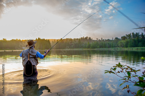 Fototapet Young man flyfishing at sunrise