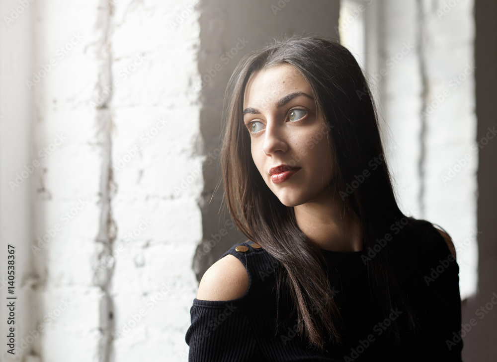 Close up portrait of young brunette female with perfect green eyes thoughtfully looking at the window. Young Caucasian woman came at love appointment, worried and waiting for her guy