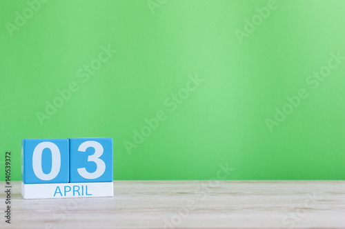 April 3rd. Day 3 of month, calendar on wooden table and green background. Spring time, empty space for text