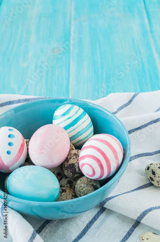 Colorful Easter Eggs on the rustic wooden background in blue bowl and linens towel. Selective focus.