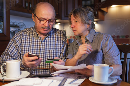 An elderly couple uses electronic payments through a smartphone and a bank card. They are afraid of fraud and an unfamiliar system of payment.