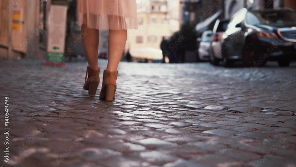 Woman walking on cobblestone pavement road. Girl exploring new city wearing in shoes and skirt. Close-up view. Woman walking on cobblestone pavement road. Girl exploring new city wearing in shoes and skirt. Close-up view.