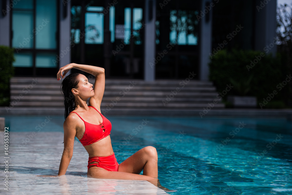 Beautiful dark hair sexy woman young girl model in sunglasses and elegant red sexy swimsuit lingerie with crystals around the pool