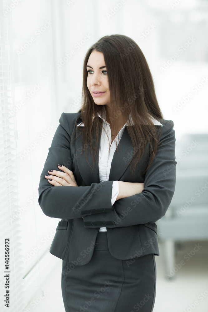 successful business woman standing near window with hands claspe successful business woman standing near window with hands claspe