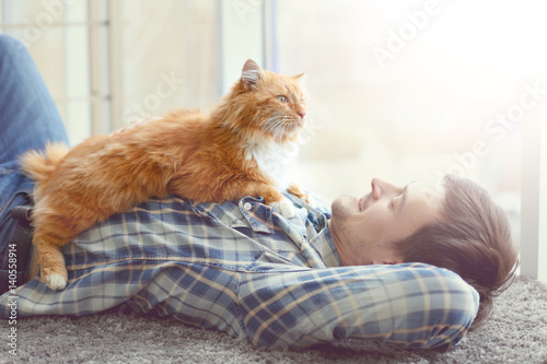 Canvas Print Young man with fluffy cat lying on a carpet