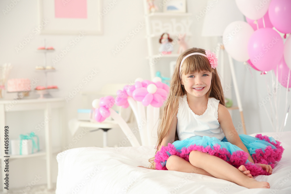 Cute girl sitting on bed in room decorated for birthday celebration Cute girl sitting on bed in room decorated for birthday celebration