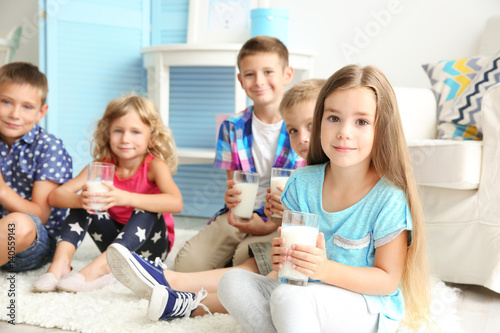 Cheerful children with glasses of milk sitting on a floor in the room