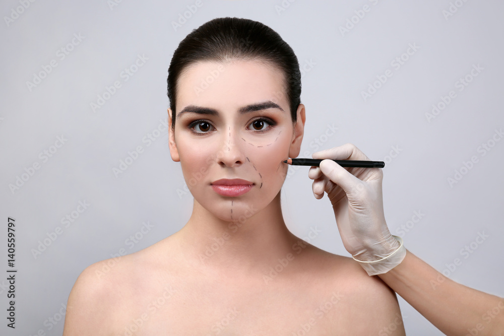 Plastic surgeon marking female face prior to operation, on light background Plastic surgeon marking female face prior to operation, on light background