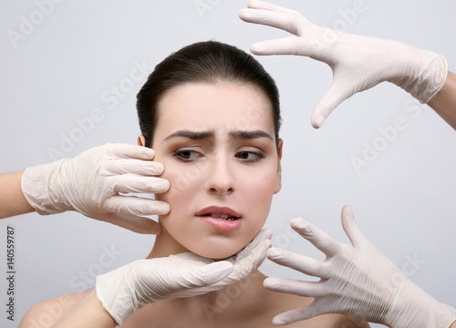 Hands in rubber gloves touching face of young beautiful woman, on light background