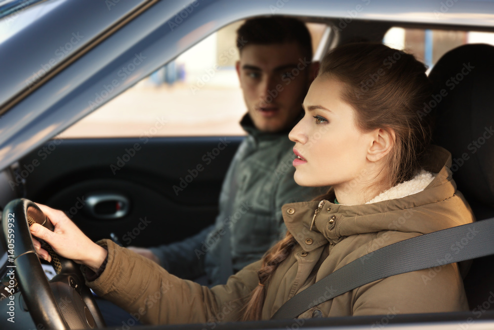 Fototapeta premium Young woman passing driving license exam while sitting in car with instructor