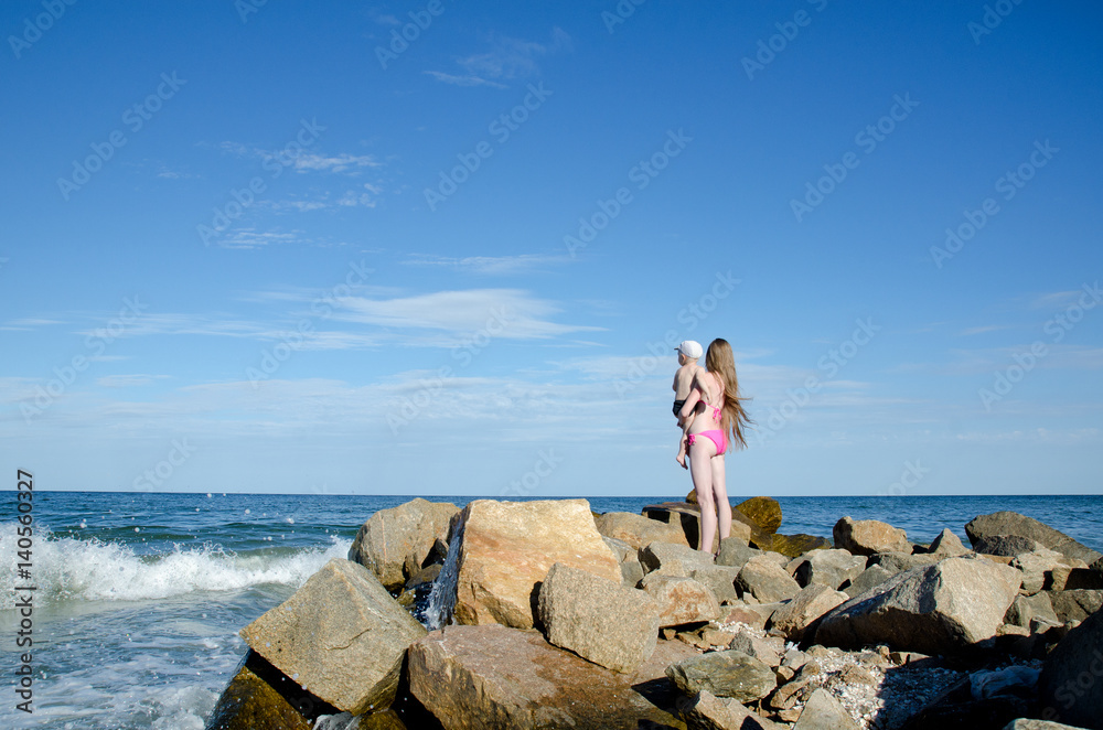 Mother with a child on the hands on the sea shore are among the stones