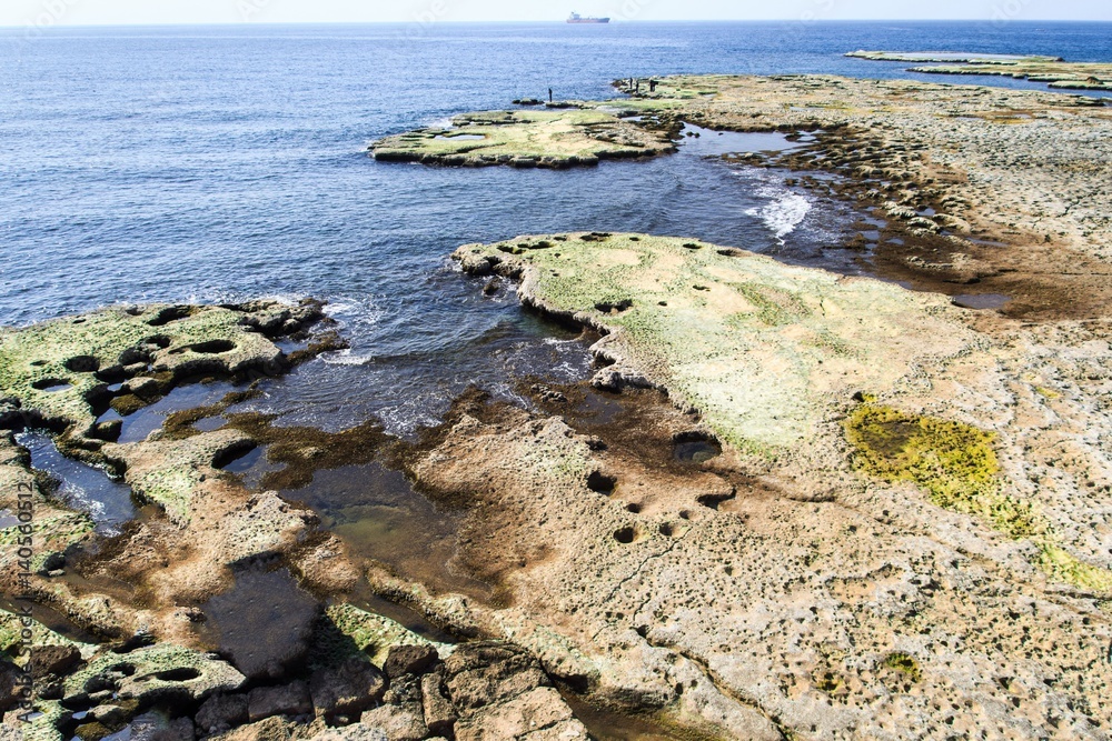Flat rocks coastline with fisherman in Byblos, Lebanon