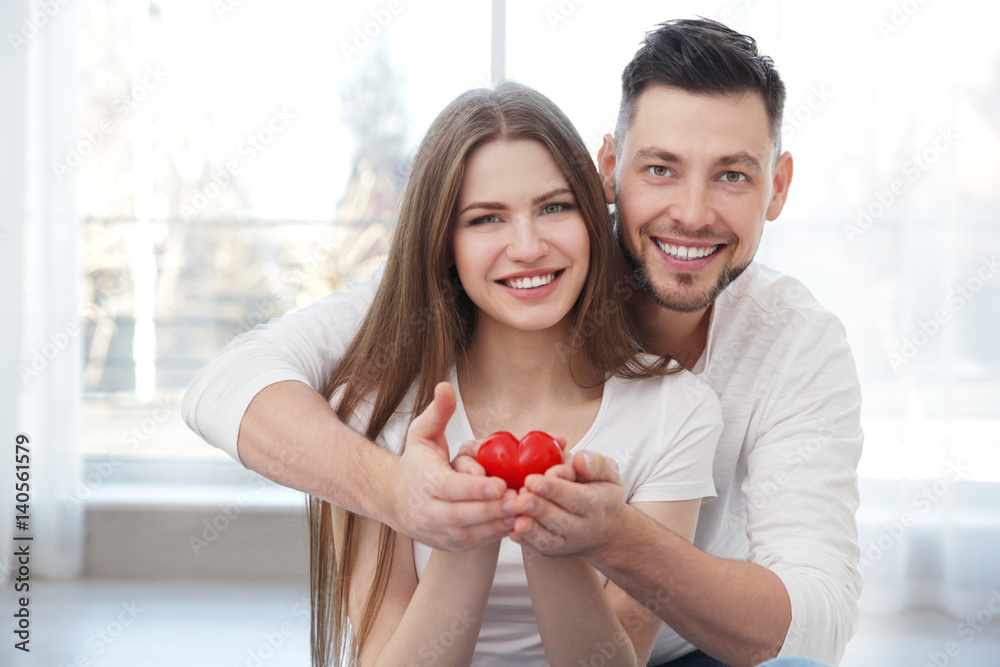 Happy young couple with small red heart at home