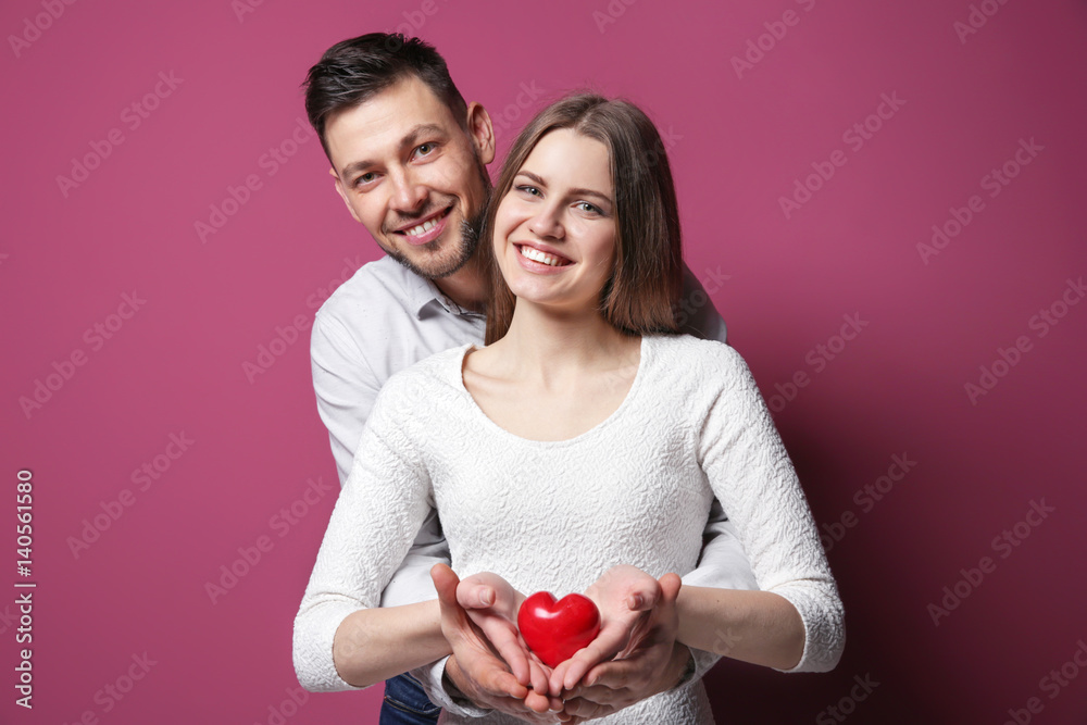 Happy young couple with small red heart on color background Happy young couple with small red heart on color background