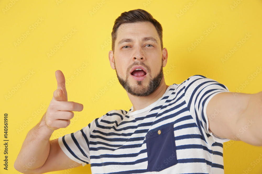 Funny young man taking selfie on color background