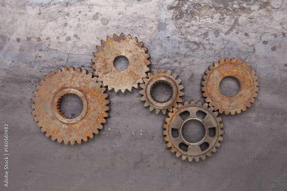 A group of five rusty gears linked together over a grungy steel background. A group of five rusty gears linked together over a grungy steel background.