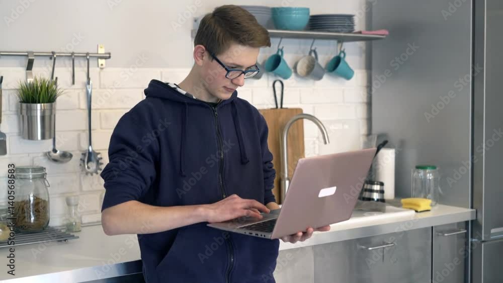 Teenage boy using laptop standing in kitchen at home
Teenage boy using laptop standing in kitchen at home