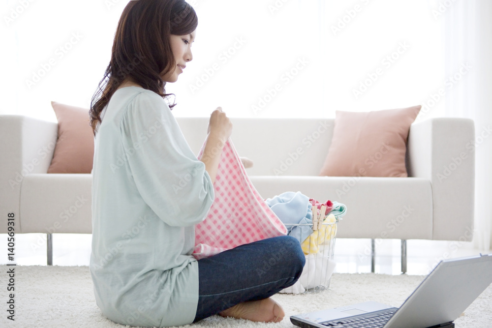 Young woman folding laundry and looking at laptop Young woman folding laundry and looking at laptop