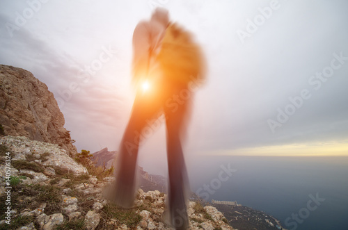 Blurred young man with a backpack on top of a mountain at sunset.