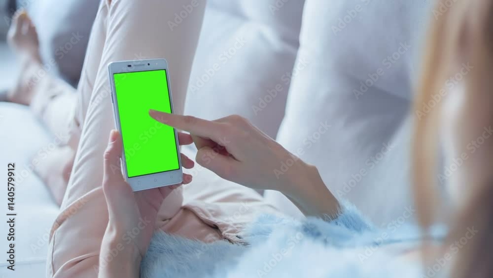 Young Woman in blue sweater laying on couch uses SmartPhone with pre-keyed green screen. Few types of gestures - scrolling up and down, tapping, zoom in and out. Perfect for screen compositing Young Woman in blue sweater laying on couch uses SmartPhone with pre-keyed green screen. Few types of gestures - scrolling up and down, tapping, zoom in and out. Perfect for screen compositing