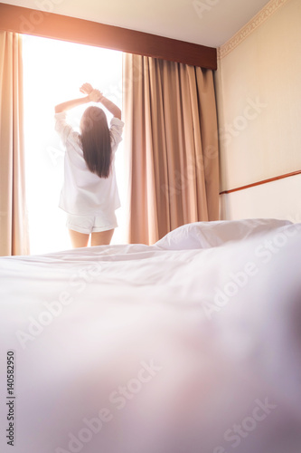 Healthy Woman stretching in bed room and open the curtains after wake up, back view, lifestyle people in cozy indoor comfortable relaxing space