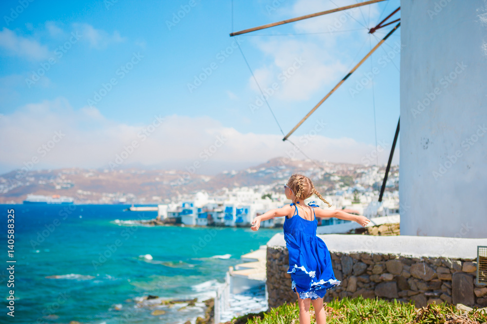 Happy little girl in front of windmills at popular tourist area on Mykonos island, Greece