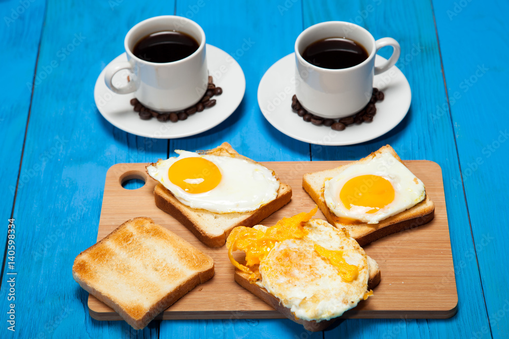 Two cups with coffee, toast and egg on a blue wooden table Two cups with coffee, toast and egg on a blue wooden table