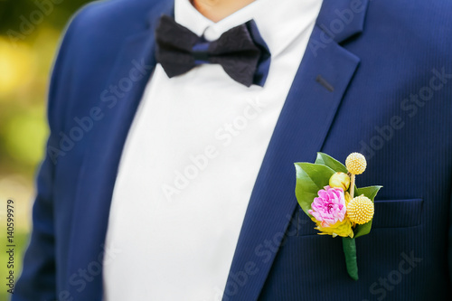 Pink peon boutonniere pinned to a grooms jacket
