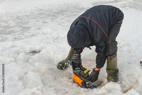 Man cutting chainsaw shell in ice