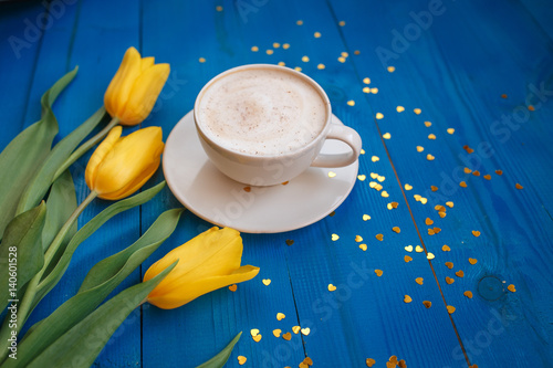 Coffee mug with yellow tulip flowers and notes good morning on blue rustic table from above, breakfast on Mothers day or Womens day .Spring  flowers bouquet photo