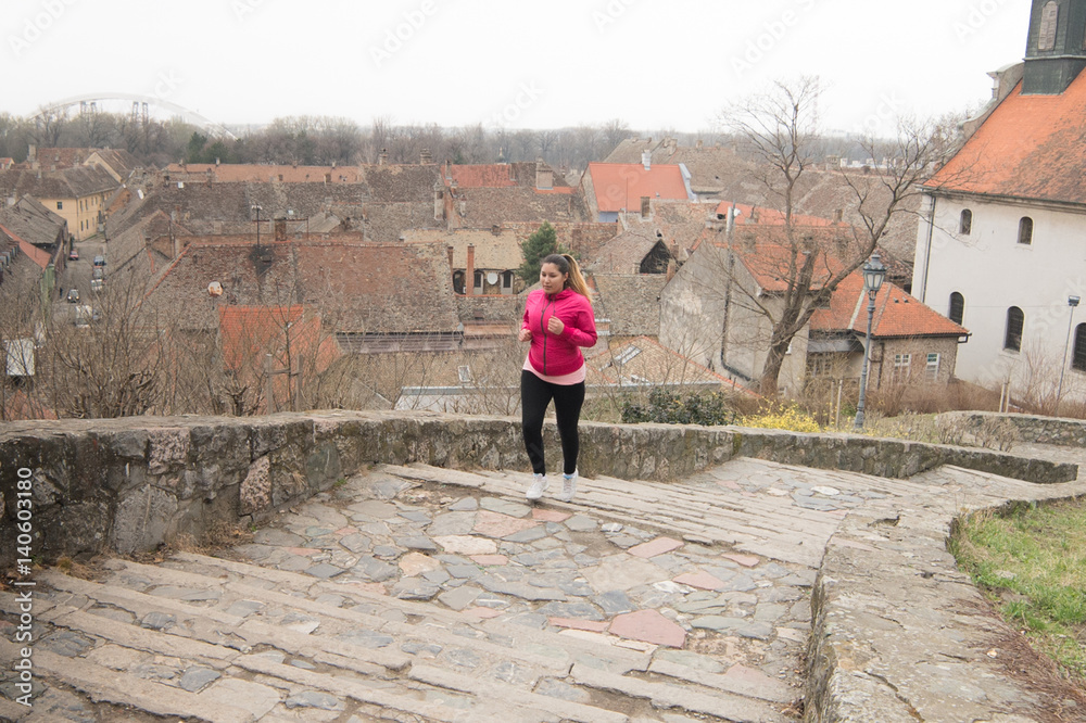 Girl wearing sportswear and running upstairs at city fortress
