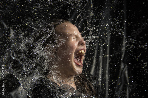 water throwing to a young girl in hands and face with black background  