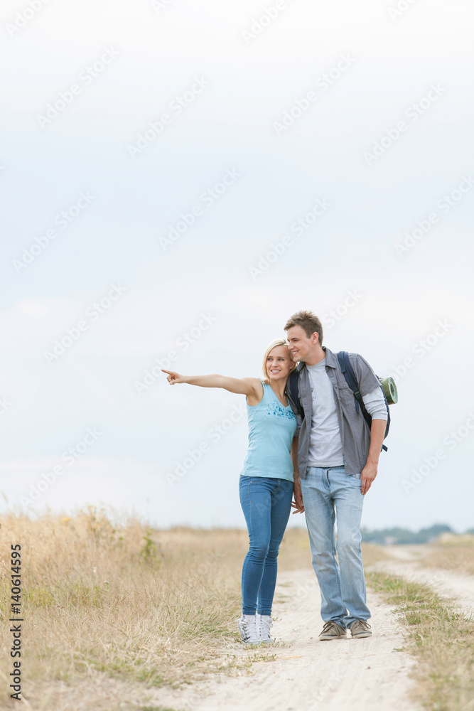 Young woman showing something to man while standing on trail at field