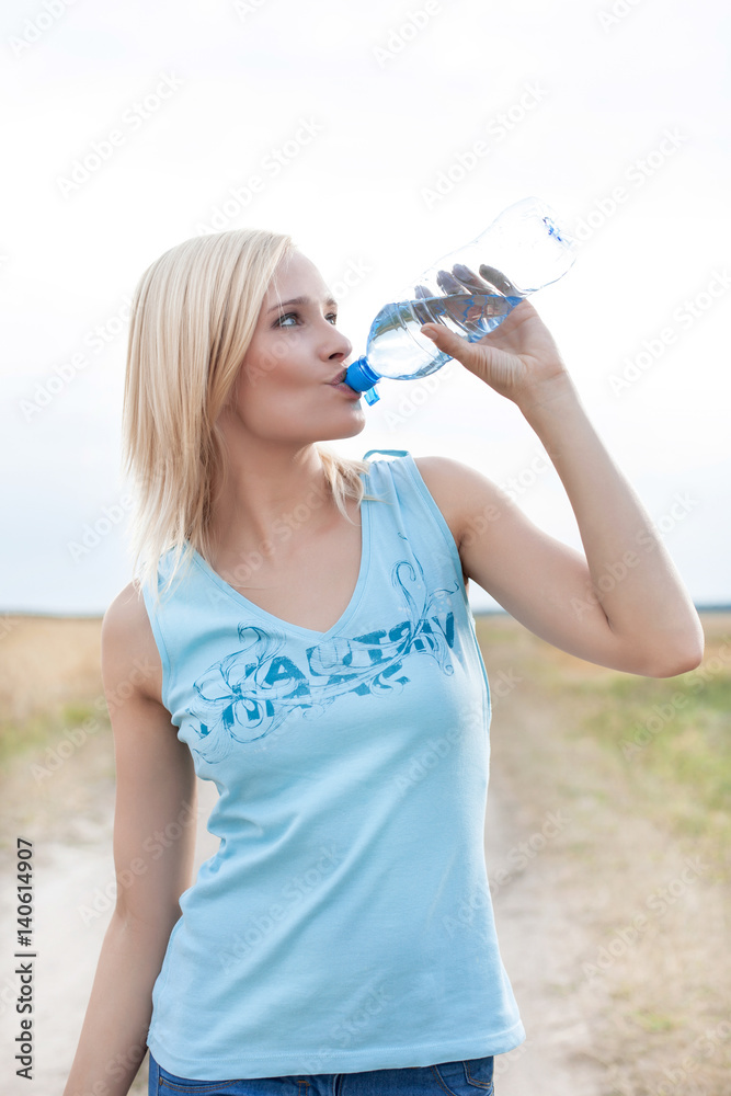 Young woman drinking water from bottle on field Young woman drinking water from bottle on field