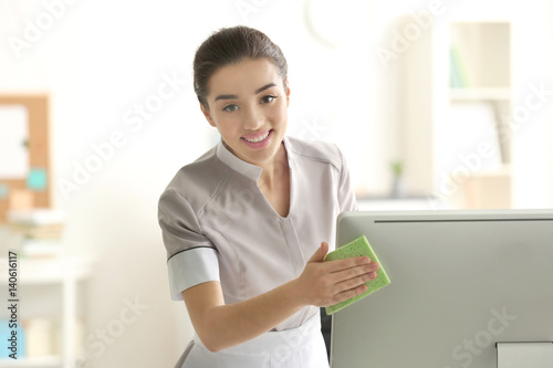 Beautiful young charwoman wiping pc monitor in office