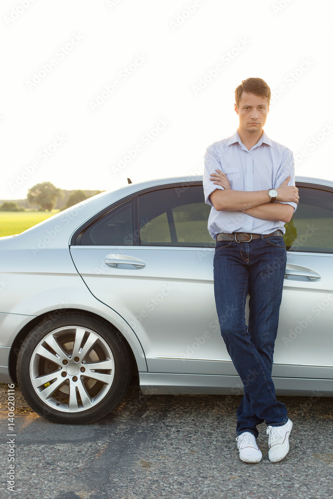 Full length portrait of young man standing by car at countryside