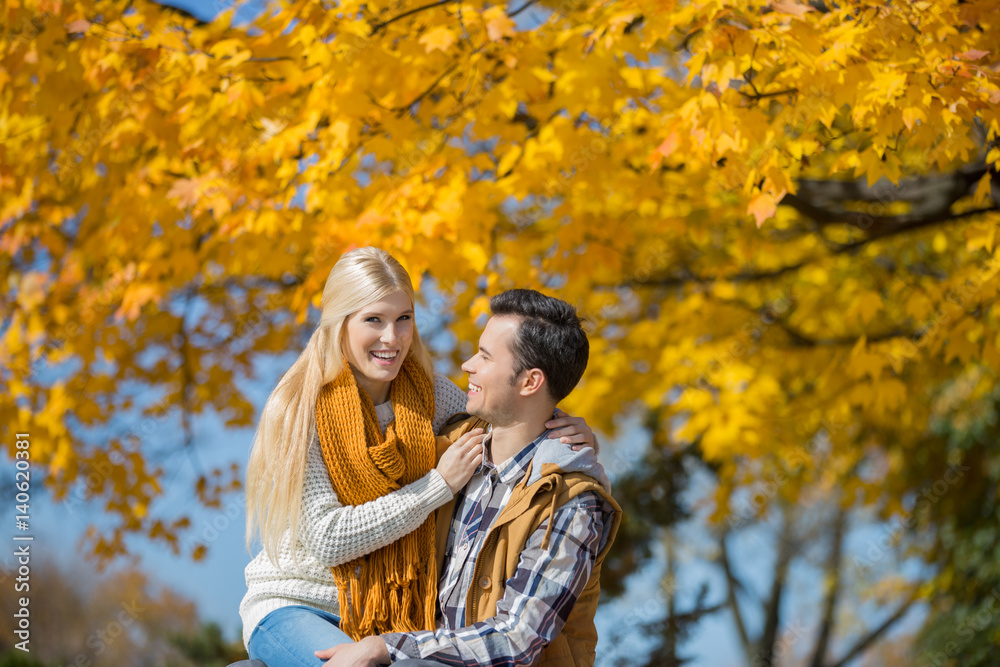 Portrait of happy woman sitting on man's lap in park during autumn