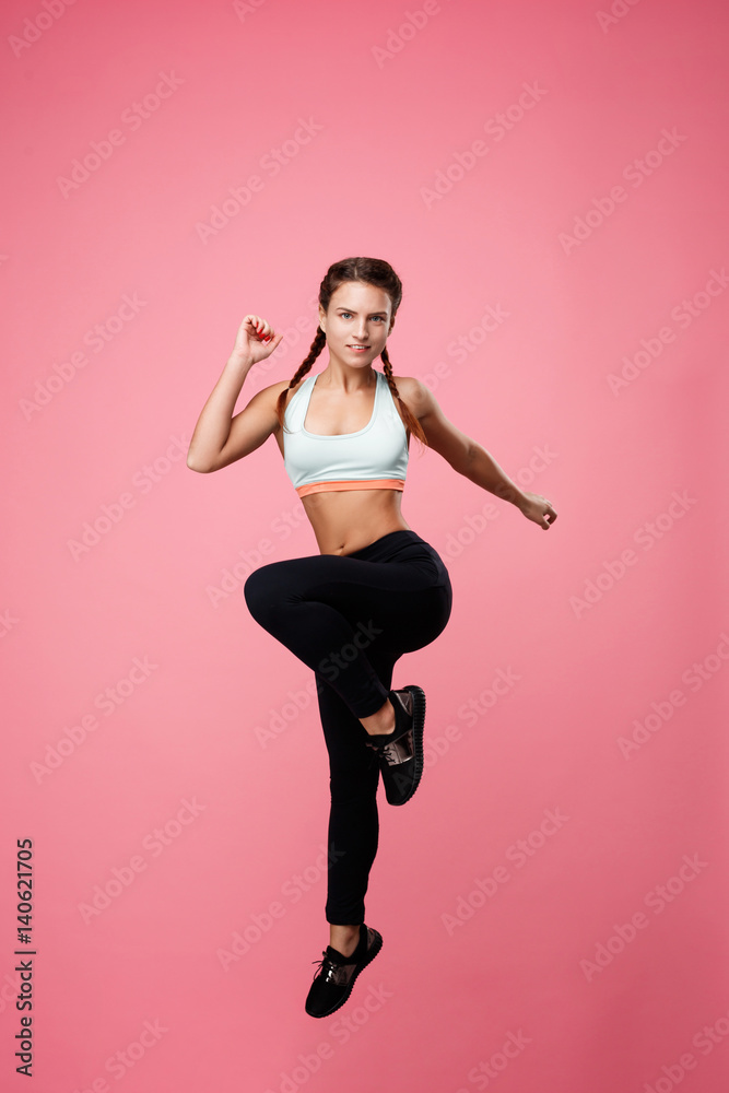 Fit woman in sport clothing jumping with left leg up 