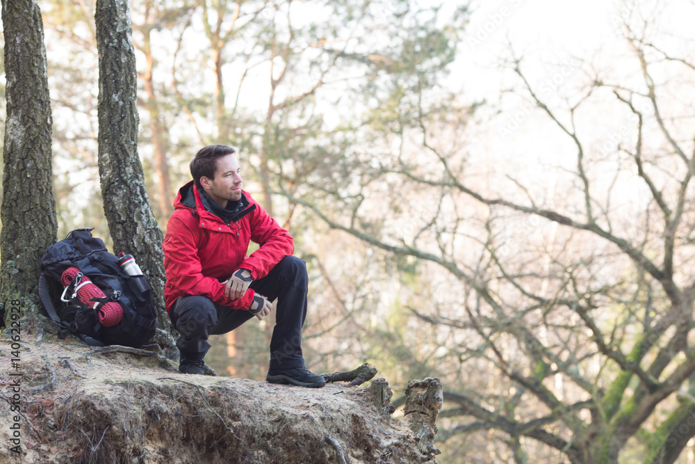 Full length of male hiker crouching on cliff in forest Full length of male hiker crouching on cliff in forest
