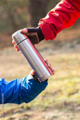 Cropped image of hikers holding insulated coffee container in forest