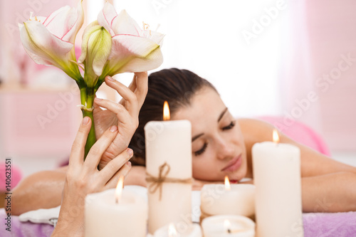 Masseur hands holding beautiful flowers behind candles. Relaxation and comfort photo