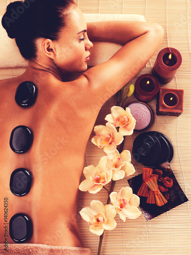 Adult woman relaxing in spa salon with hot stones on body