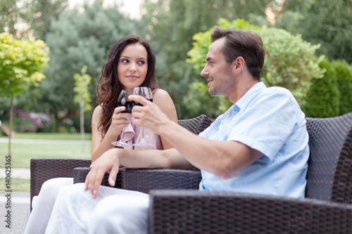 Loving young couple toasting red wine on chairs in park