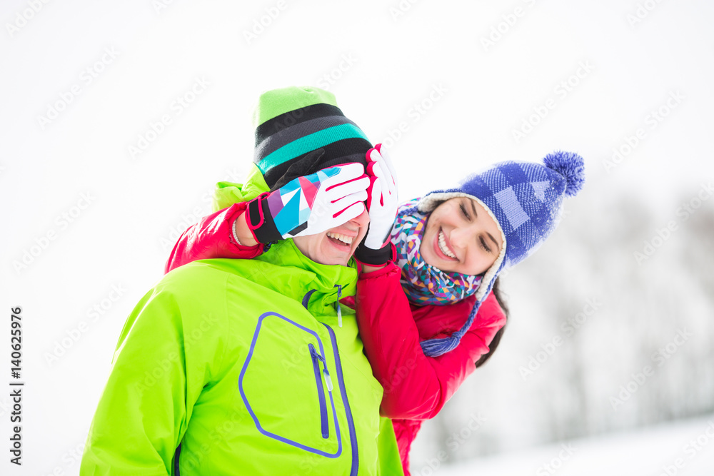 Smiling young woman covering man's eyes in winter Smiling young woman covering man's eyes in winter